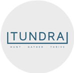 The image features the logo for "TUNDRA," which is written in blue, uppercase letters with a horizontal line beneath it. Below the line, there are the words "HUNT," "GATHER," and "THRIVE" in smaller, blue uppercase letters, separated by dots. The background is light gray.