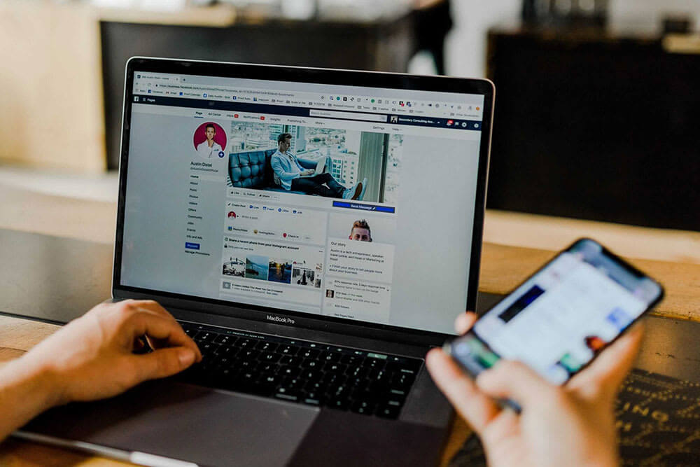 A person surfing on social media on a laptop with a mobile device in hand