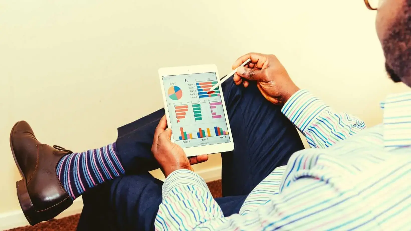 Man analyzing colorful graphs and charts on a tablet using a stylus, dressed in business attire.