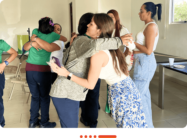 A group of people engage in warm embraces and laughter in a bright, casual indoor setting, showcasing friendship and connection.
