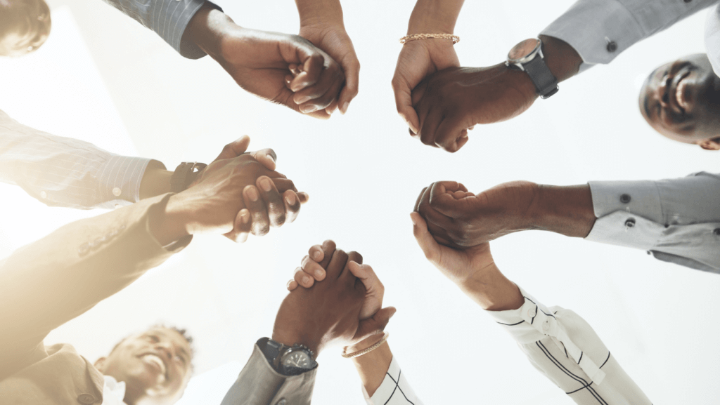 A group of people holding each other's hands in a circle, viewed from below. The image highlights unity and teamwork, showing diverse individuals collaborating and supporting each other. The bright PENTA background emphasizes a positive and hopeful atmosphere.