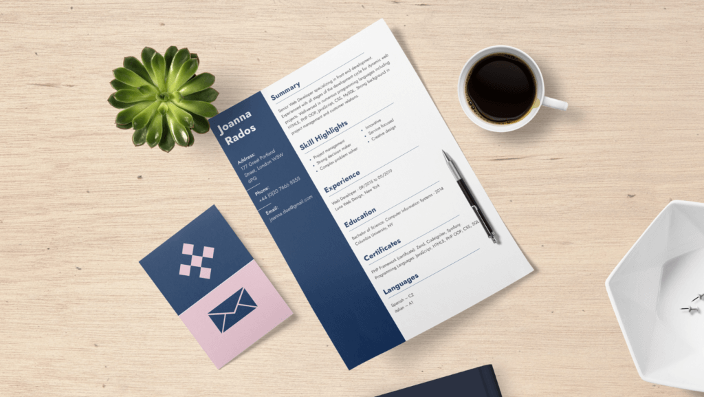 A resume with the name Joanna Rados is placed on a wooden desk. The resume highlights summary, skills, experience, education, certificates, and languages. Nearby are a steaming cup of coffee, a pen, a succulent plant, an envelope with a note inside, and an eye-catching geometric dish.