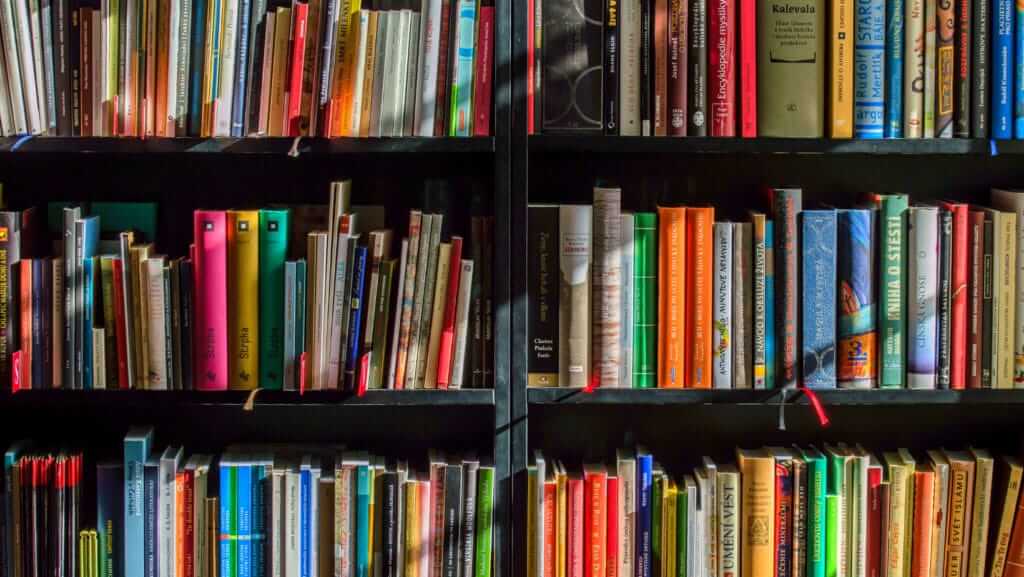 A colorful array of books neatly arranged on black bookshelves. The collection includes a wide variety of genres, with training courses and other books of various sizes and colors creating a vibrant and organized display. Some titles are facing outward, making them easily readable.