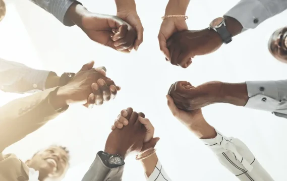 Diverse team holding hands in unity, symbolizing teamwork, inclusion, collaboration, and workplace diversity from a low angle view