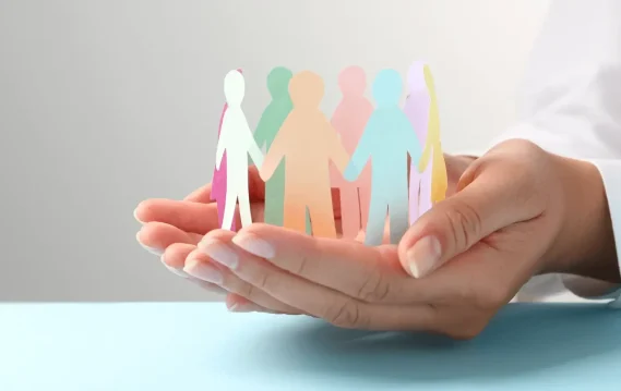 Hands holding a circle of colorful paper cutout people, representing unity, diversity, and community support